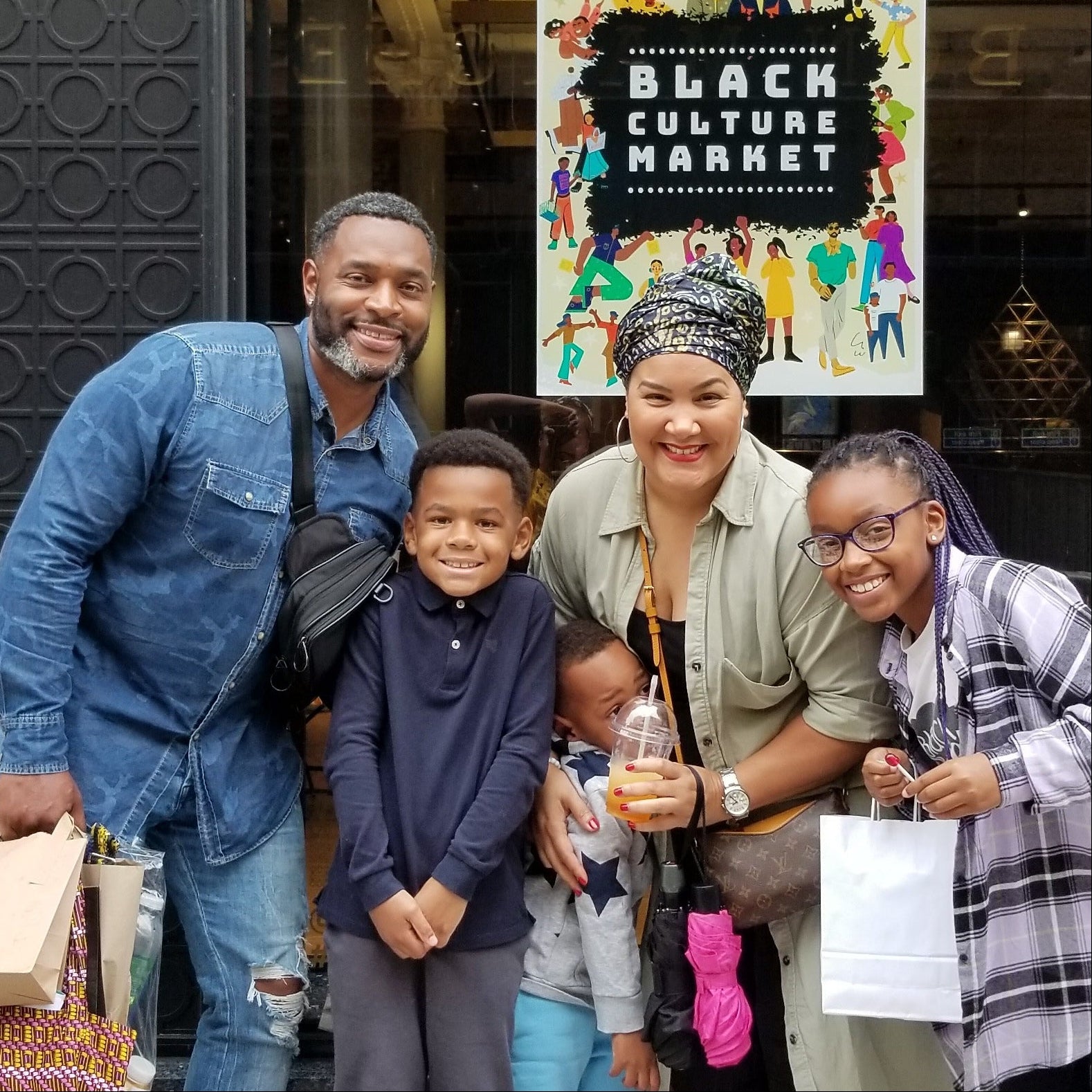 Family of five posing in front of a building with a 'Black is Beautiful Market' sign.